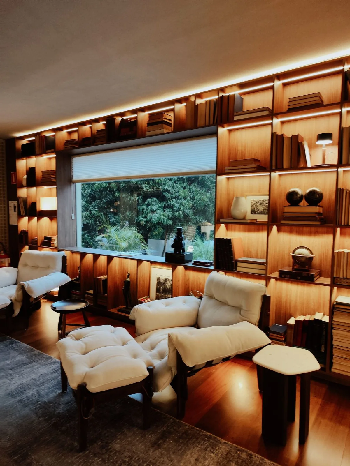Sala com biblioteca iluminada e poltronas claras