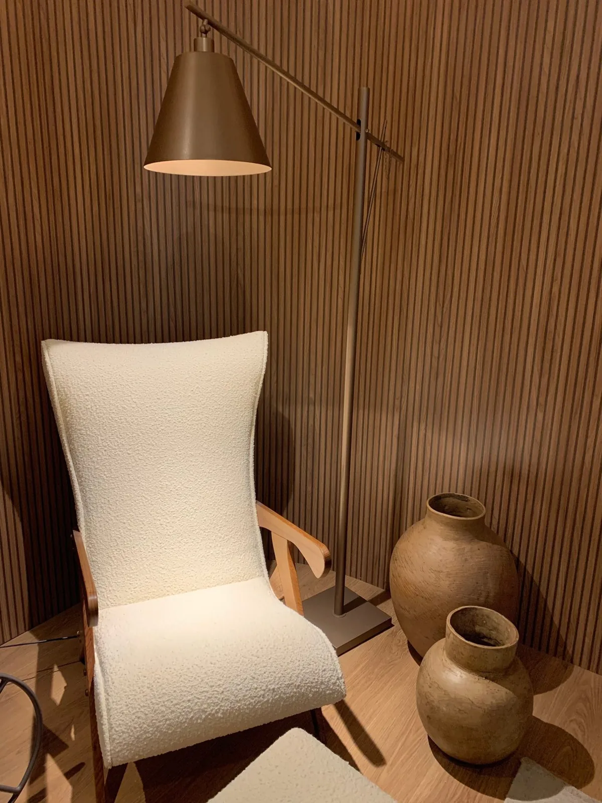 Poltrona clara ao lado de uma luminária e vasos de barro