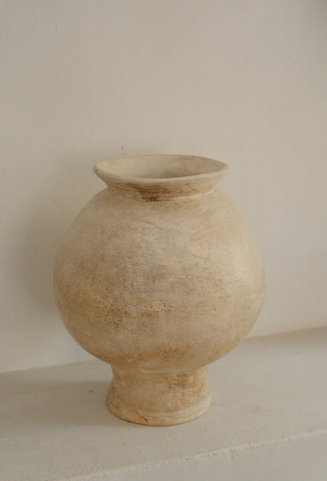 Um vaso de barro claro, sozinho, sob uma luz suave